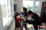 刘军正在通过望远镜向远处的林海四处瞭望，王娟在旁边记录 张桂芹 摄 - 中国新闻社河北分社