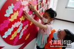 图为在志愿者的帮助下，小朋友将自己的小心愿粘贴在“心愿墙”上。 李栋 摄 - 中国新闻社河北分社